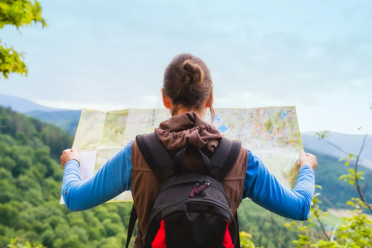 Woman traveler with backpack checks map to find directions in wilderness area